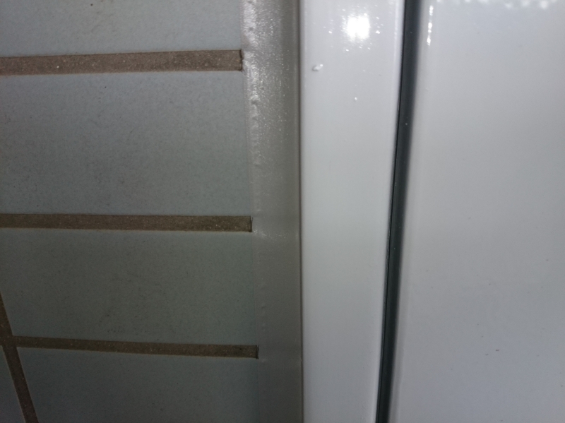 マンションの共用廊下内、タイル面とパイプシャフト扉枠の間に施工された線防水（シーリング）の例。